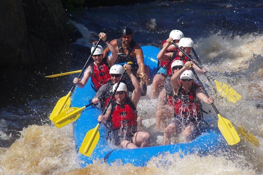 A group of people in a blue raft navigating through whitewater rapids. 3