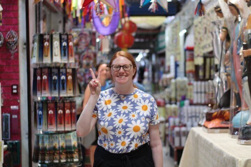 A person in a flower-patterned shirt in a market with shelves of items and hanging decorations. 4