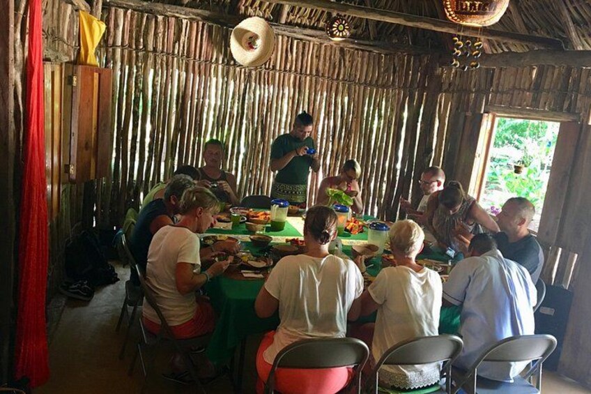 A group of people dining at a rustic wooden table with a thatched roof. 3