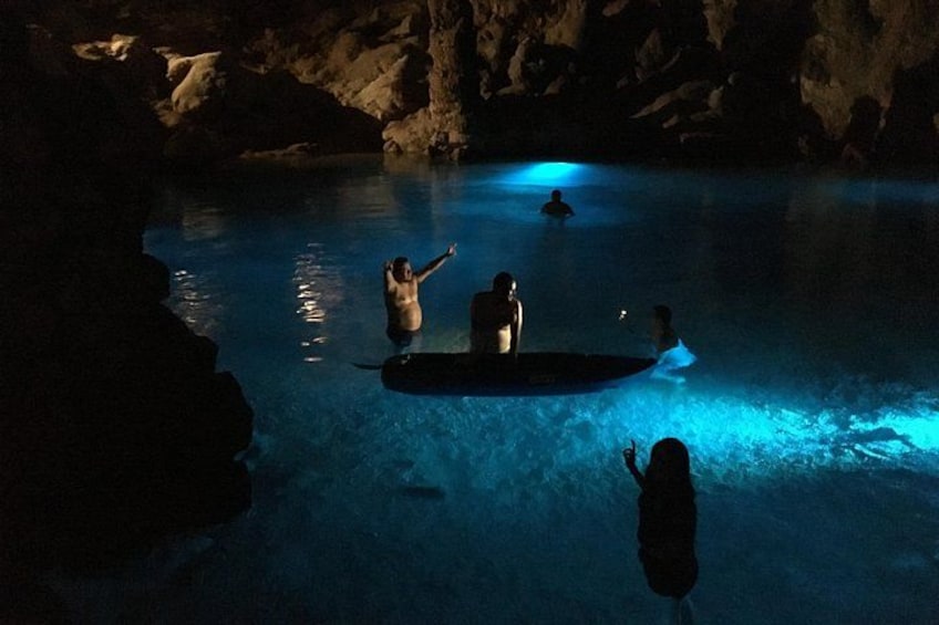 A cave with a swimming pool, people in the water, and a person on a paddleboard. 4
