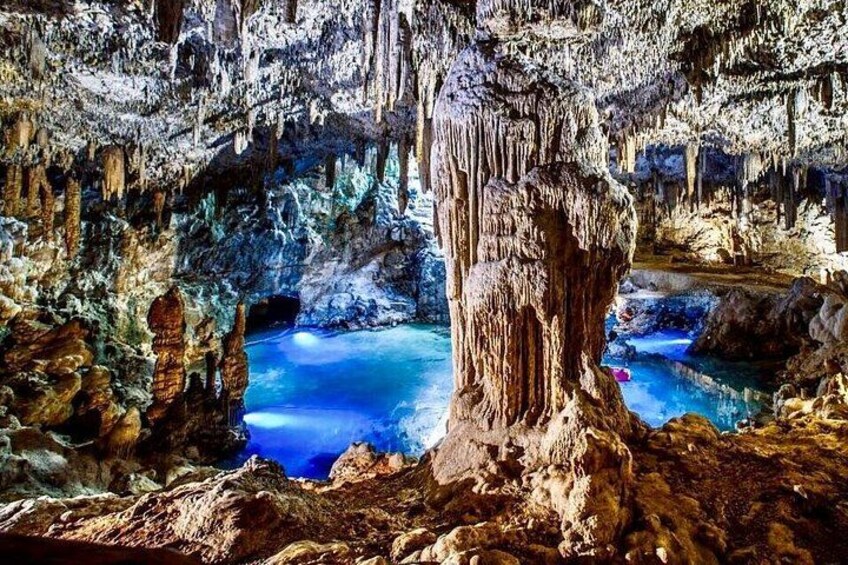 A cave with stalactites, stalagmites, and a blue pool. 5