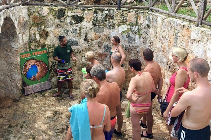 A group of people gathered around a stone structure with a sign that reads 'ZAZIL TUNICH.' 2