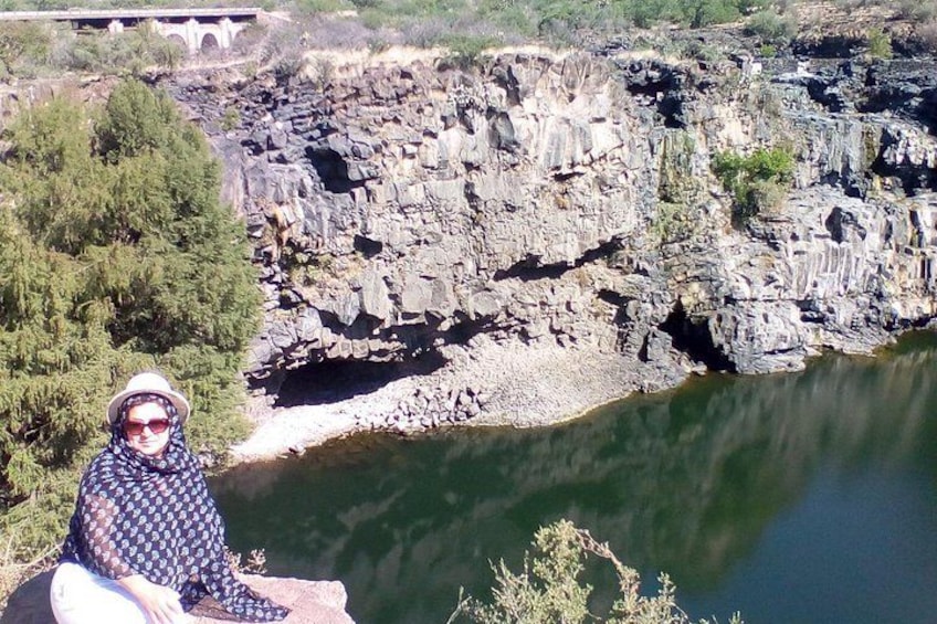 A person sitting by a river with rocky cliffs in the background. 1