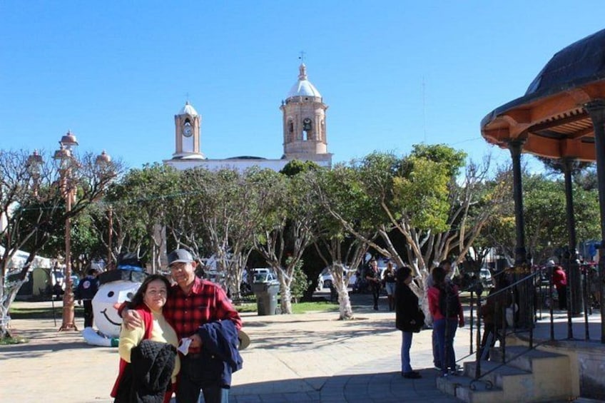 A plaza with a clock tower, trees, and people. 4
