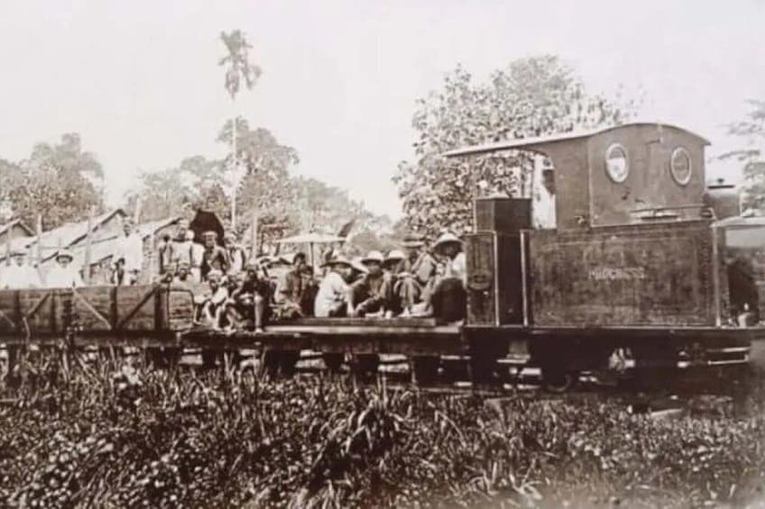 A vintage train with passengers, surrounded by a field. 2
