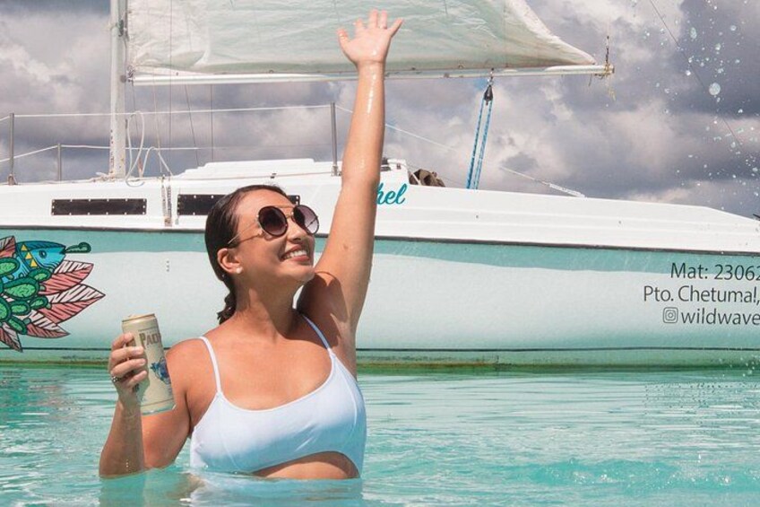 En person i en vit baddräkt som håller i ett glas, stående i en pool med en båt i bakgrunden. 4