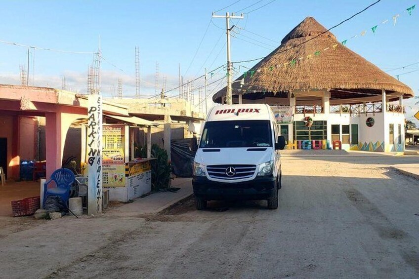 A white van parked in front of a building with a thatched roof, a sign for 'HOLPAX', and a small kiosk. 5