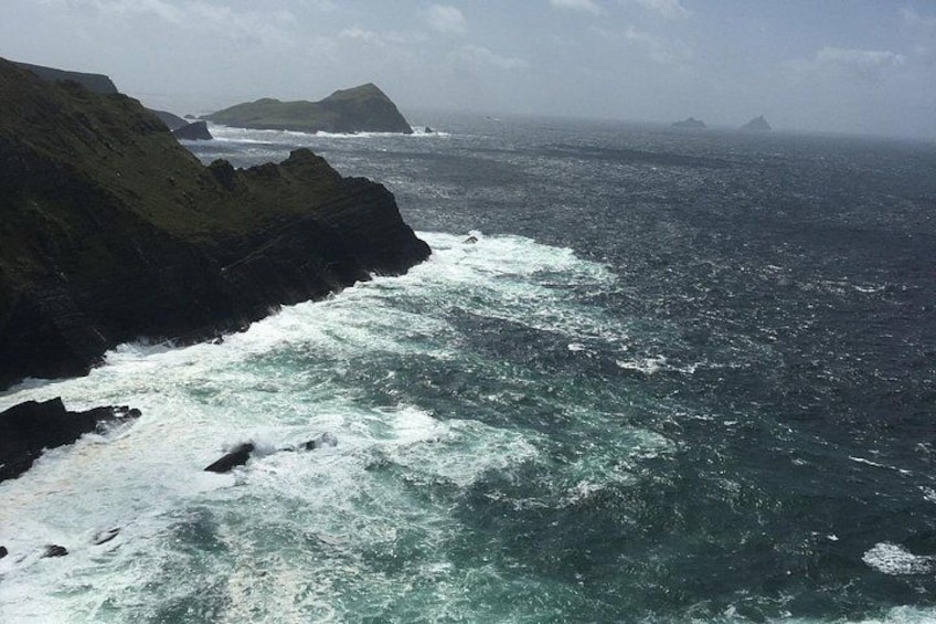 Una costa escarpada con olas rompiendo contra acantilados pronunciados y una isla distante. 3