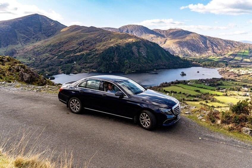 Un coche negro estacionado en una carretera con paisaje montañoso y un lago al fondo. 1