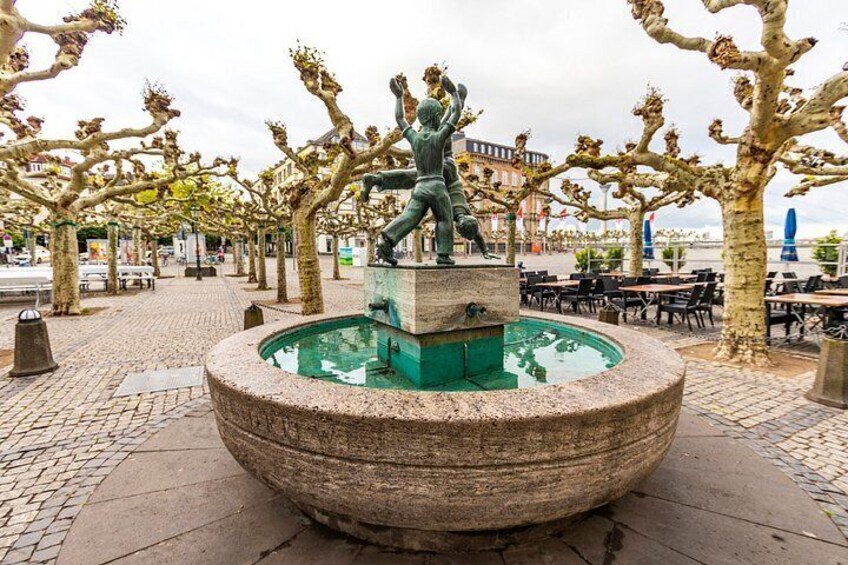 A fountain with a statue in a public square surrounded by trees. 5