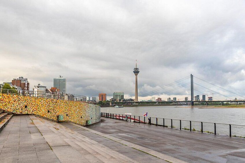 A waterfront promenade with a bridge, a tower, and a cityscape in the background. 3