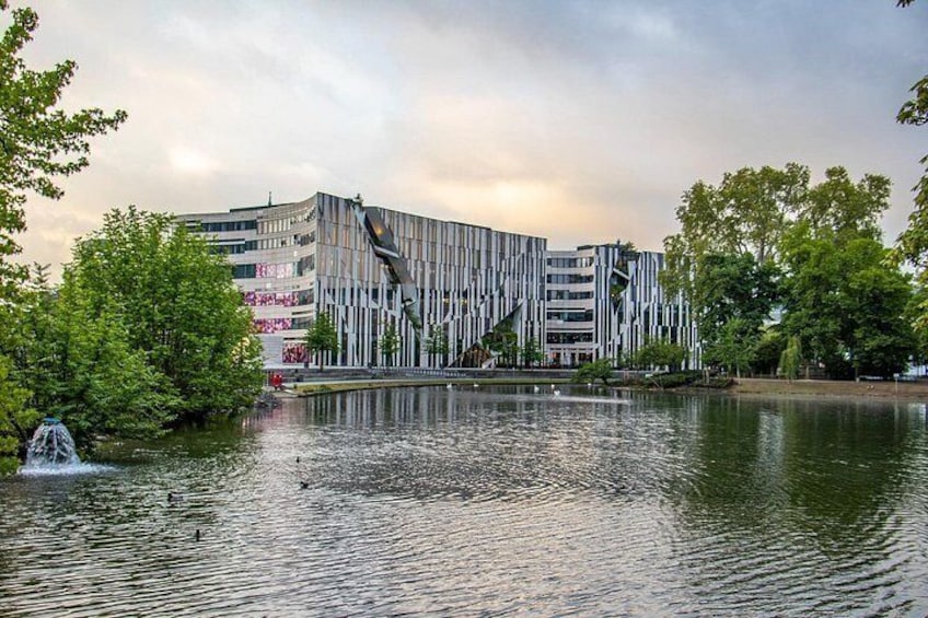A modern building with vertical lines, a body of water, and trees. 4