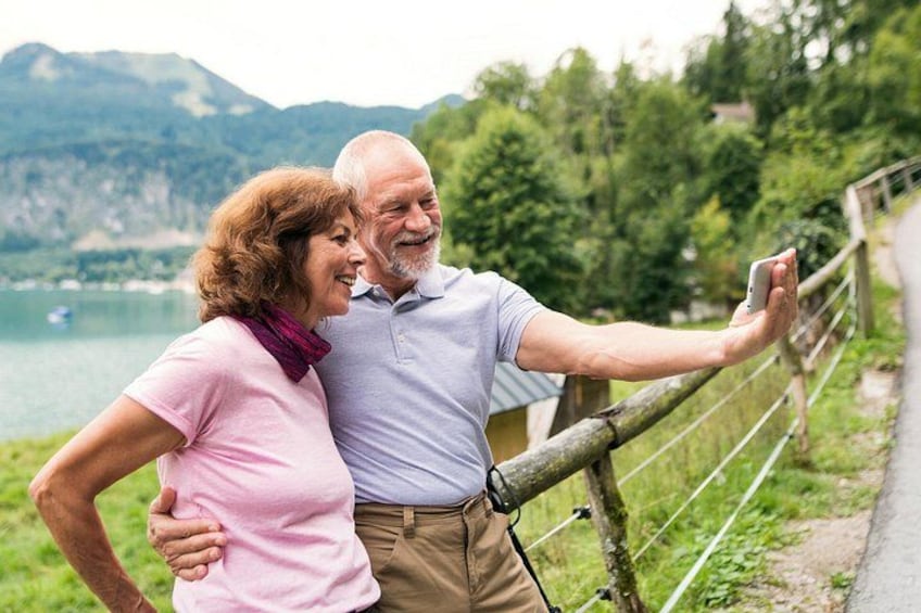Un couple prend un selfie sur un sentier au bord d’un lac, avec des montagnes en arrière-plan. 4