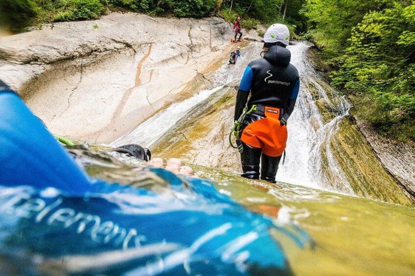 A person in a wetsuit and helmet preparing to rappel down a rocky waterfall. 3