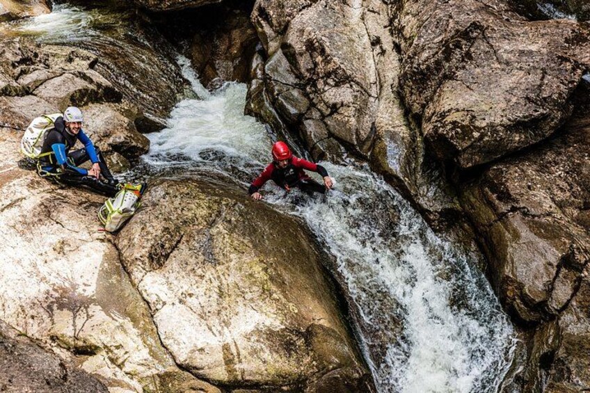 Two people in helmets and protective gear near a fast-flowing river in a rocky gorge. 5