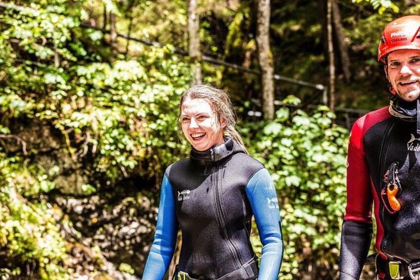 Two people in wetsuits standing in a forested area. 2