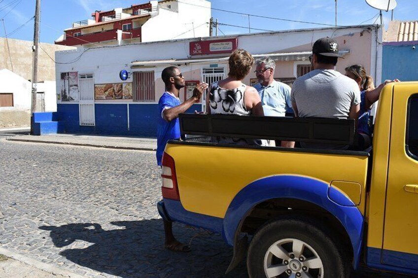 A yellow pickup truck with a blue stripe parked on a cobblestone street. 1