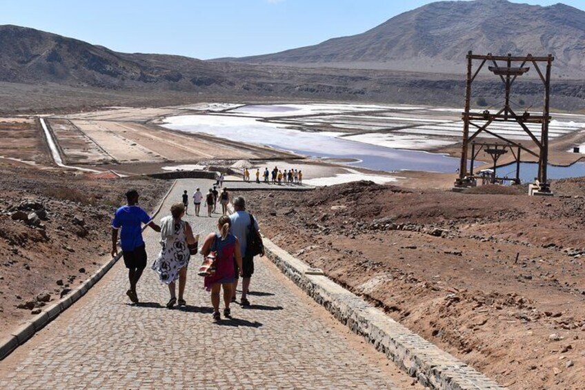 A paved pathway leading to a salt flat with a large metal structure in the background. 2