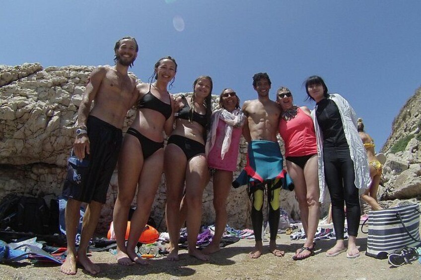 A group of people standing on a rocky beach with some wearing swimsuits and others in casual clothing. 4