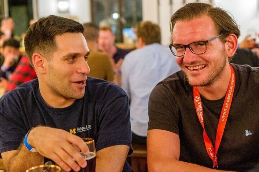Two men sitting at a table, one holding a glass. 3