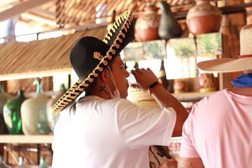 Una persona con sombrero y camisa blanca, de pie en un entorno rústico con cerámica y construcciones de madera. 5