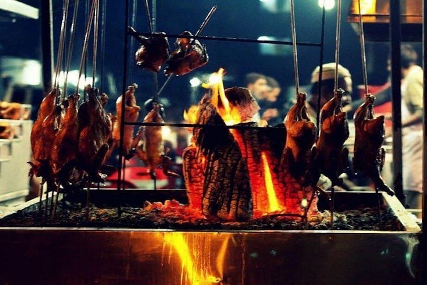 A traditional outdoor cooking setup with multiple chickens being roasted over an open flame. 4