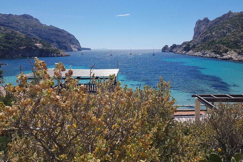 A coastal landscape with a wooden pier, clear blue sea, and rocky cliffs. 3