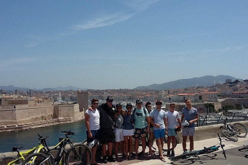 A group of people standing on a waterfront with bicycles and a cityscape in the background. 1