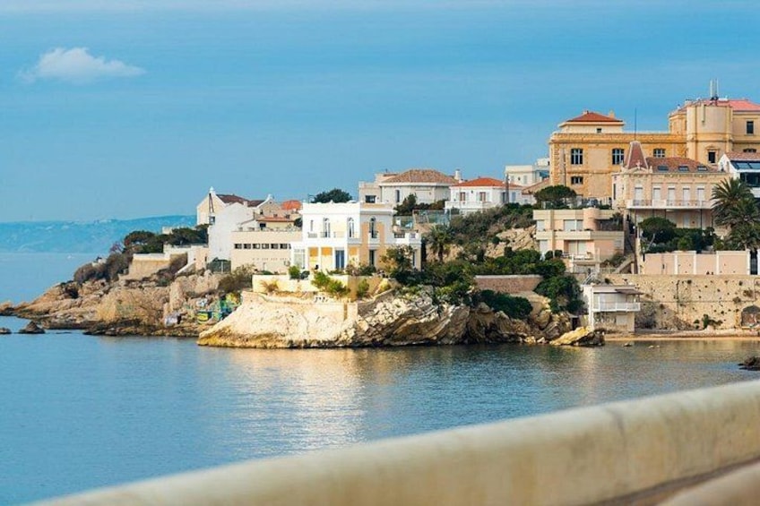 A coastal town with buildings on a rocky outcrop, calm sea, and clear sky. 2