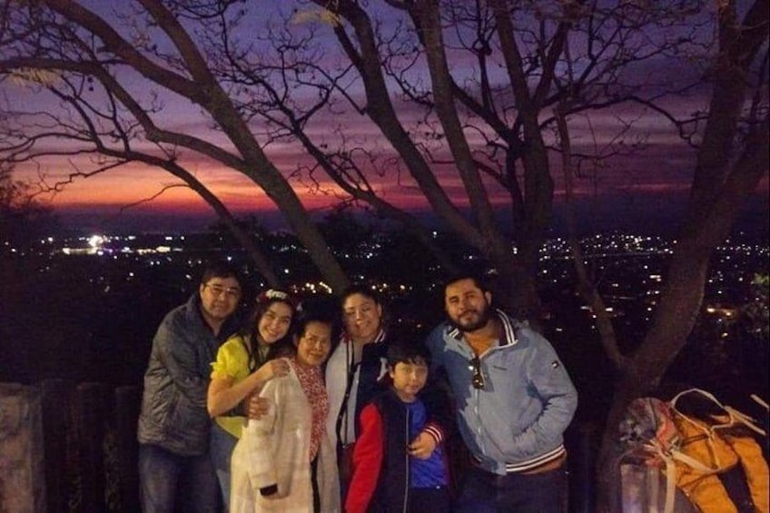 Un grupo de personas posando bajo un árbol, con un paisaje urbano de fondo. 1