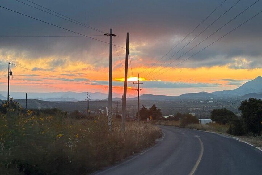 A road curving through a landscape with a sunset, mountains, and power lines. 3