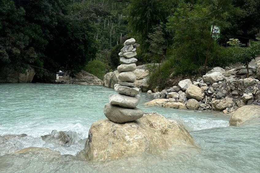 A stack of stones in a river surrounded by rocks and greenery. 5