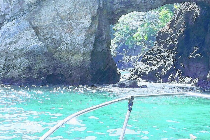 A boat in turquoise waters with a rocky cliff and a natural arch formation. 5