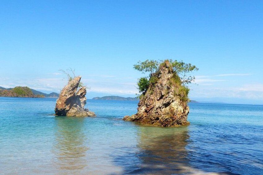 Two rocky formations in clear water with a distant landmass. 3