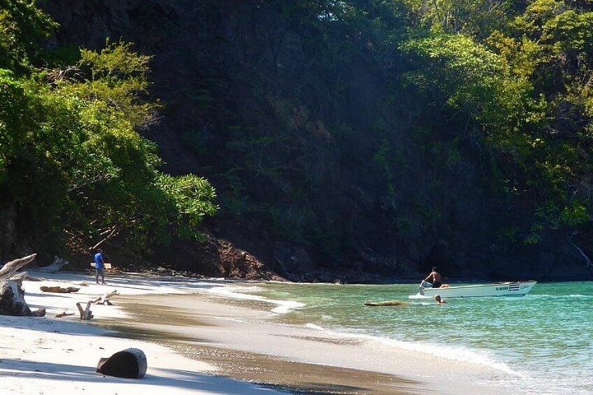 A beach with clear turquoise water, a person swimming, and a boat in the distance. 4