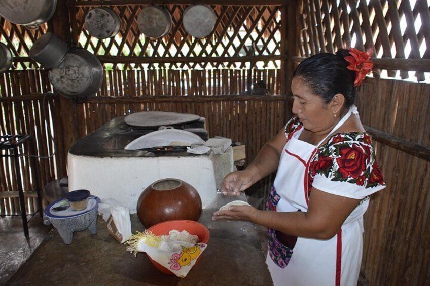 Una persona preparando comida en una cocina rústica con una olla de barro grande, una estructura de madera y utensilios de cocina tradicionales. 3