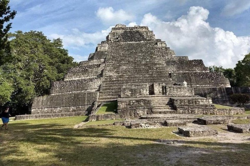 A large ancient pyramid structure with a stepped design, surrounded by grassy areas and trees. 1