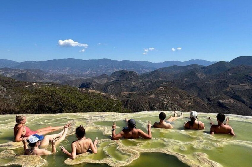 Menschen entspannen in wasserreichen Mineralbädern vor einer bergigen Landschaft. 2