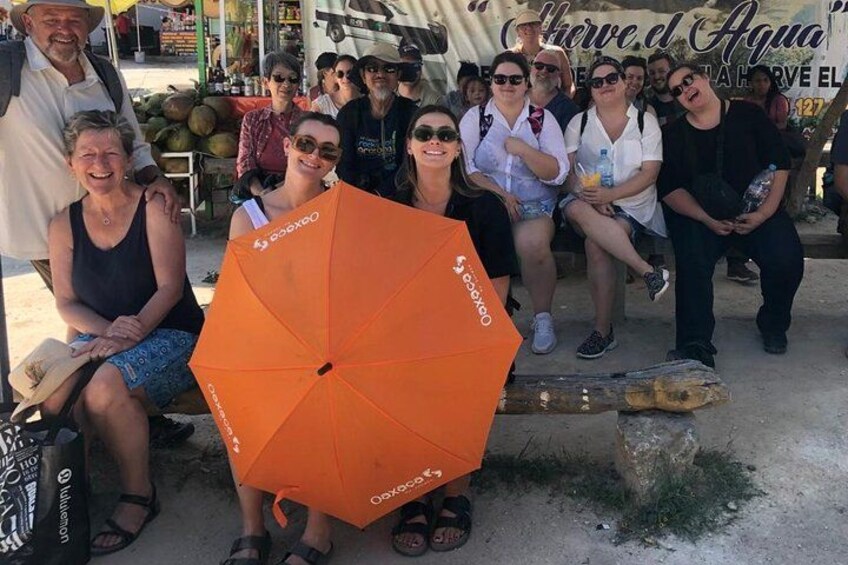 A group of people sitting on a bench with an orange umbrella in the foreground. 3
