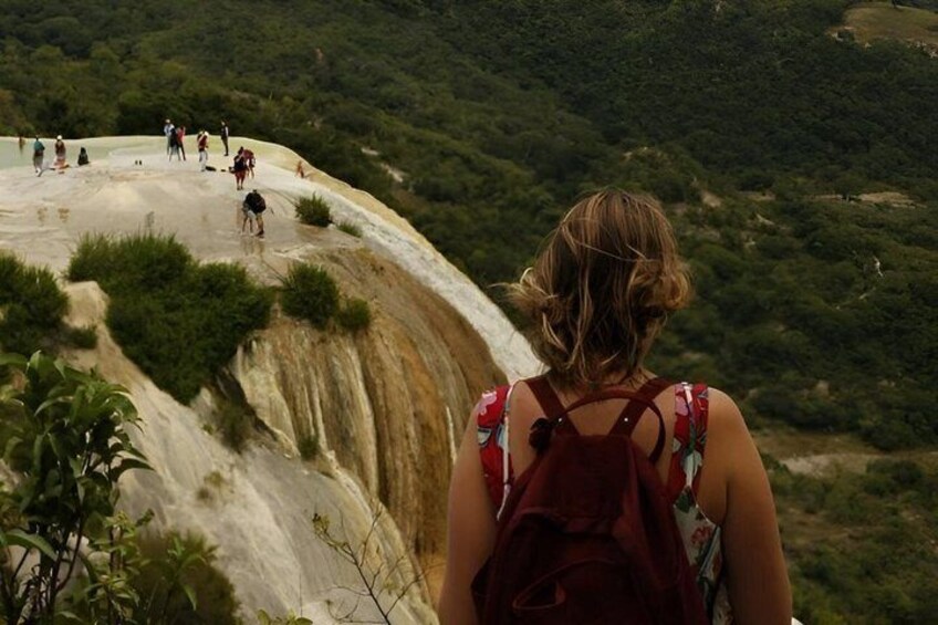 Ein Wanderer mit Rucksack geht auf einem Pfad durch üppige, grüne Landschaft und felsiges Gelände. 3