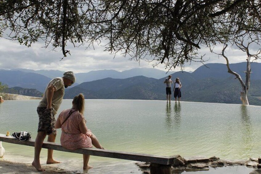 A lake with people standing and sitting on a dock, surrounded by mountains. 2