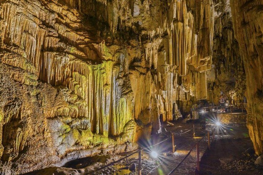 A cave with stalactites and stalagmites, a pathway, and visitors. 3