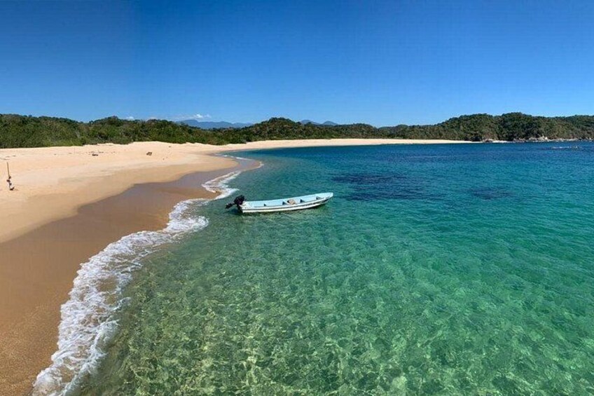 Una playa con agua turquesa cristalina, un bote en la orilla y una playa arenosa con vegetación al fondo. 4