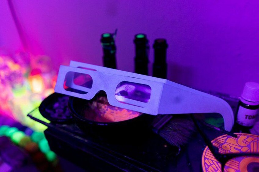 3D glasses on a table with colorful lights and a bottle labeled 'TOM' in the background. 2