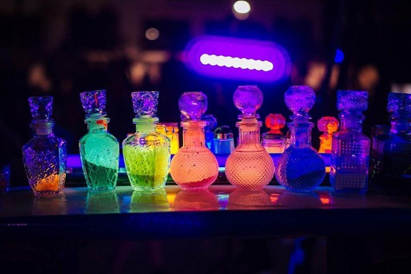 A row of colorful glass bottles with a purple neon sign in the background. 3
