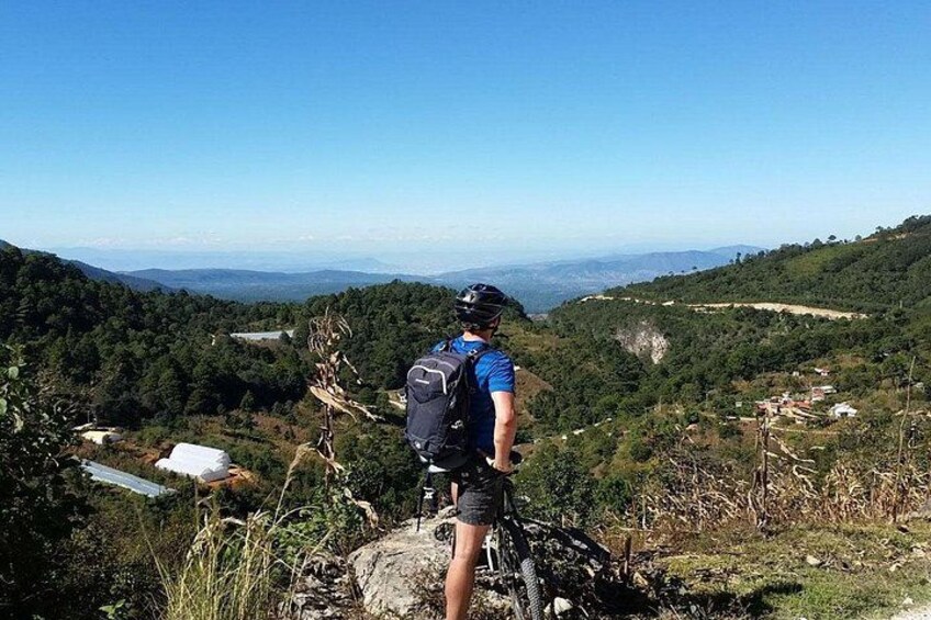 Une personne se tient sur une colline, à côté d’un vélo, et surplombe une vallée parsemée de maisons et de verdure. 2