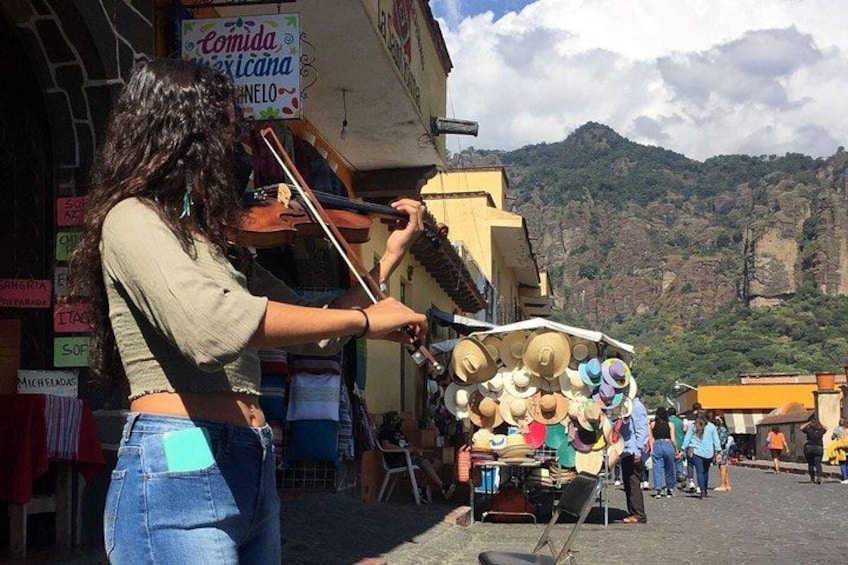 A street musician playing a violin, a hat vendor, and a mountainous backdrop. 1