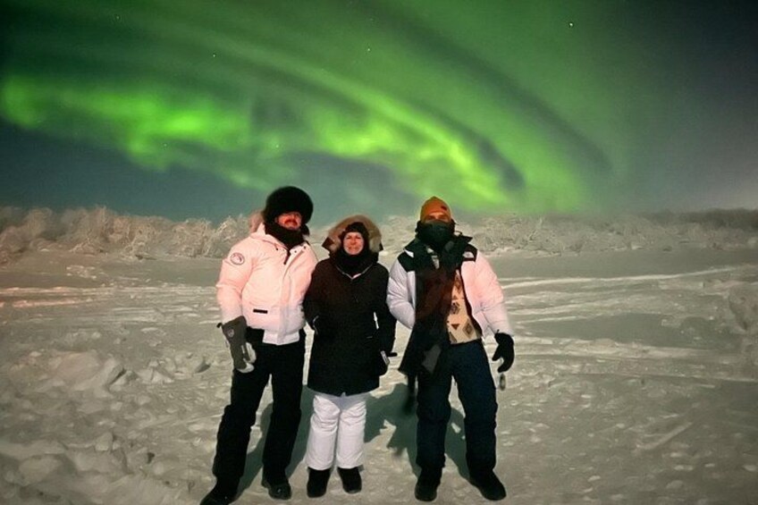 Three people standing on a snowy landscape with the aurora borealis in the background. 5