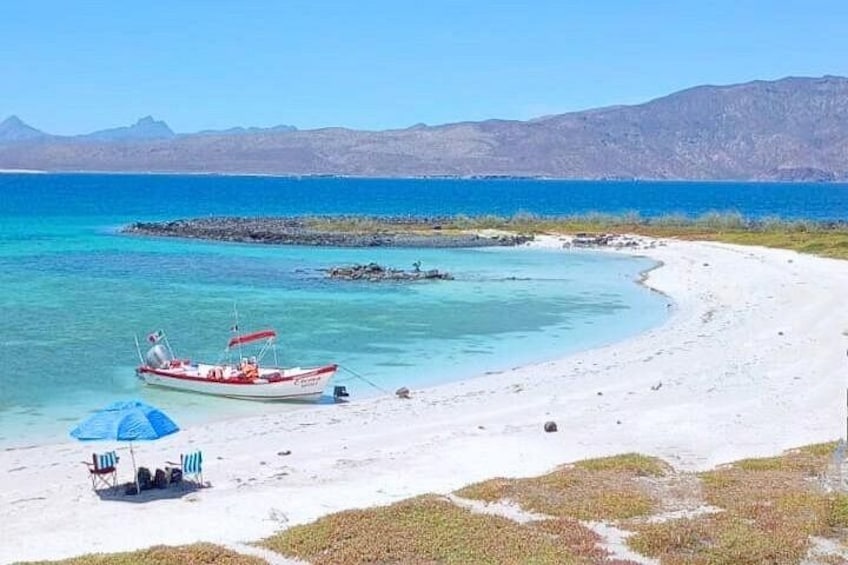 Una playa con un bote, un mar azul cristalino y montañas a lo lejos. 2
