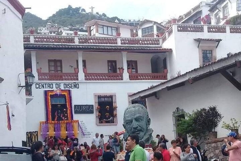 A crowded outdoor event with a building labeled 'CENTRO DE DISEÑO' and a statue in the foreground. 2